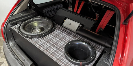 Eingebauter Subwoofer im Kofferraum eines roten Autos mit Verstärker und Verkabelung