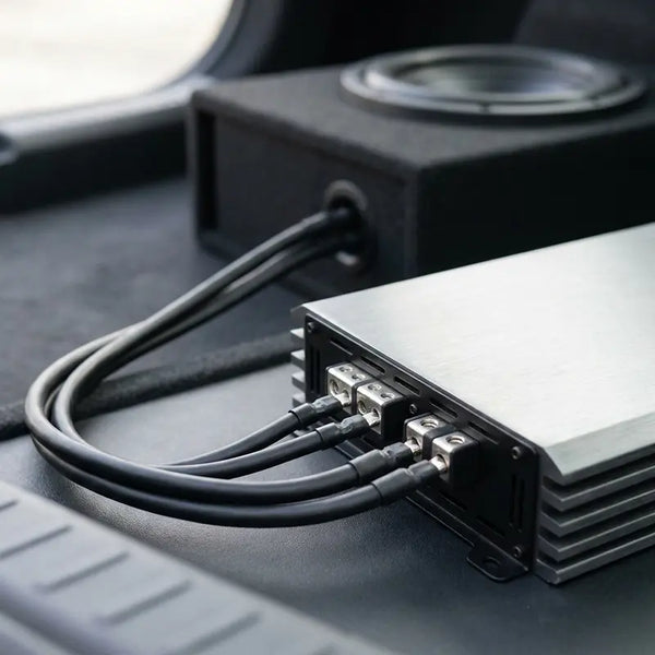 Endstufe mit Anschlussklemmen verbunden mit Subwoofer-Gehäuse im Kofferraum