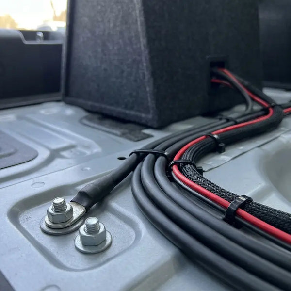 Massepunkt mit Ringösen und sauber verlegten Kabeln bei Subwoofer-Installation im Kofferraum